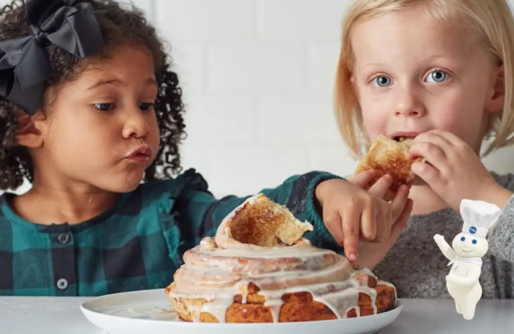 Two little girls eating a cinnamon roll.